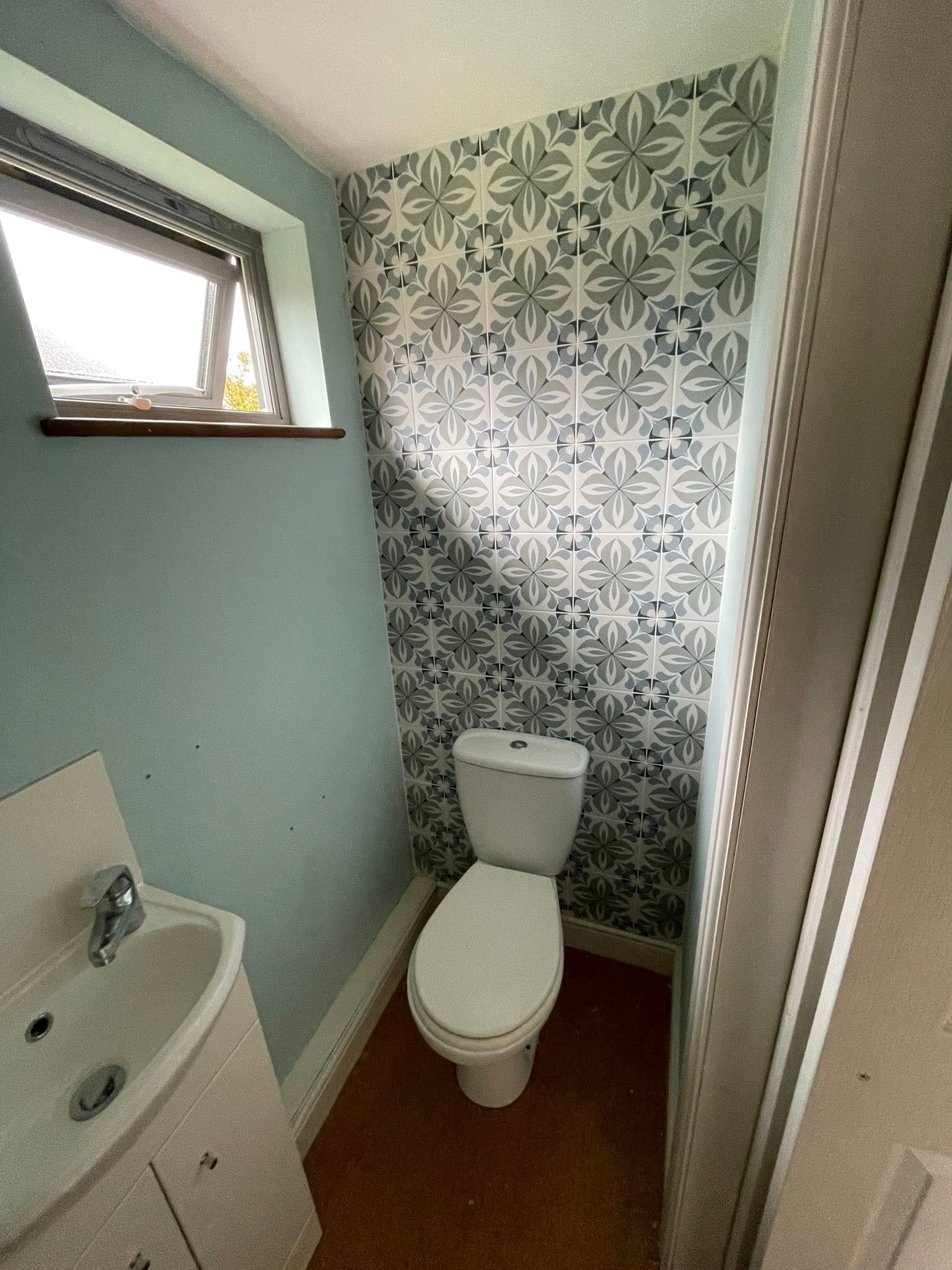 Cloakroom with fitted toilet and basin against a patterned tile wall